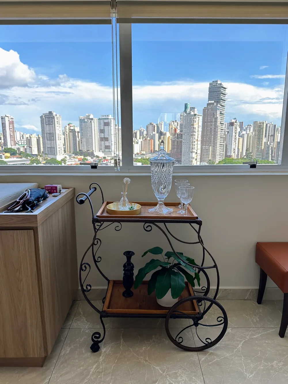A janela com o céu e os prédios de Goiânia e, diante dela, o carrinho de ferro trabalhado com peças de cristal e uma planta.